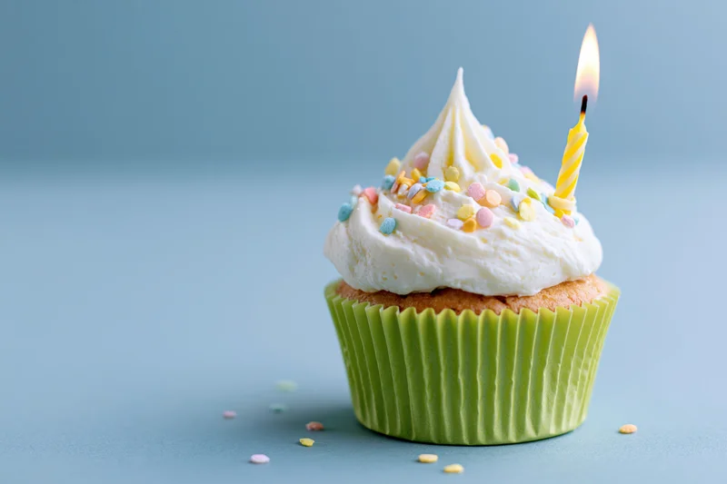 Single birthday cupcake with lit candle and sprinkles in green paper wrapper on blue surface