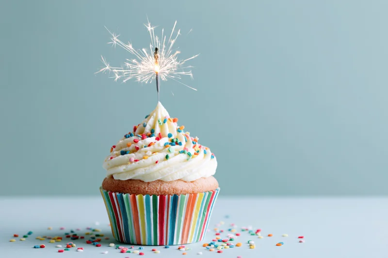 Single birthday cupcake with lit sparkler and colorful sprinkles on a striped paper wrapper