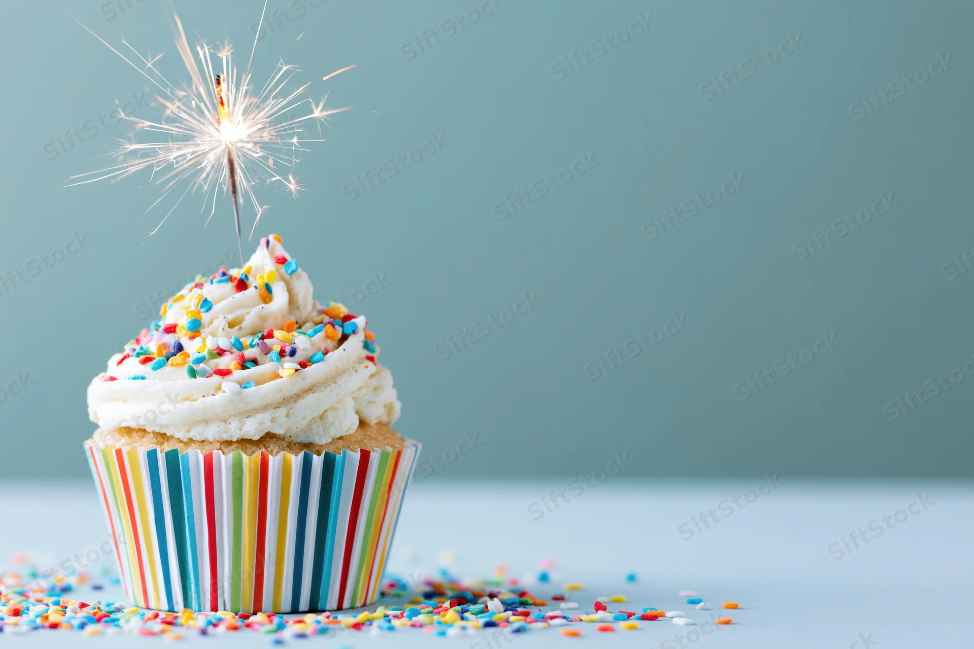 Birthday cupcake with lit sparkler and colorful sprinkles on a plain surface