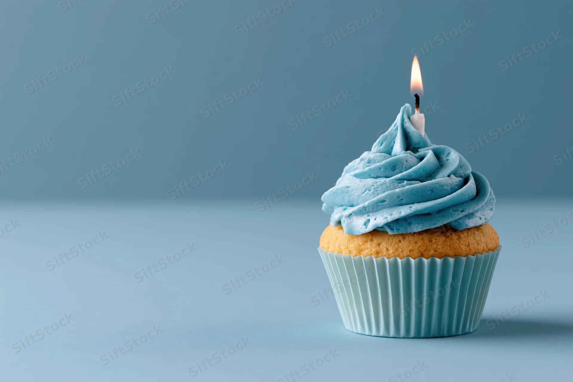 Single birthday cupcake with swirled blue frosting and lit candle on plain blue surface