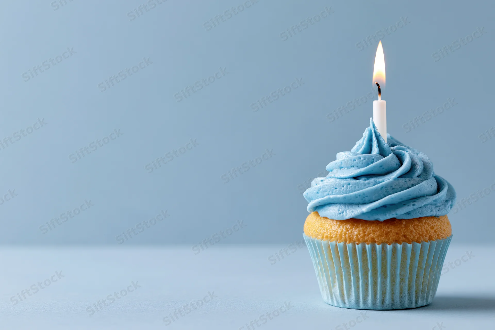 Single birthday cupcake with blue swirled frosting and lit candle on light blue surface