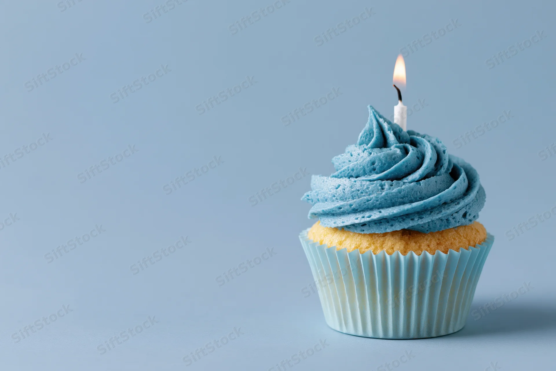 Single blue-frosted cupcake with lit candle on plain background