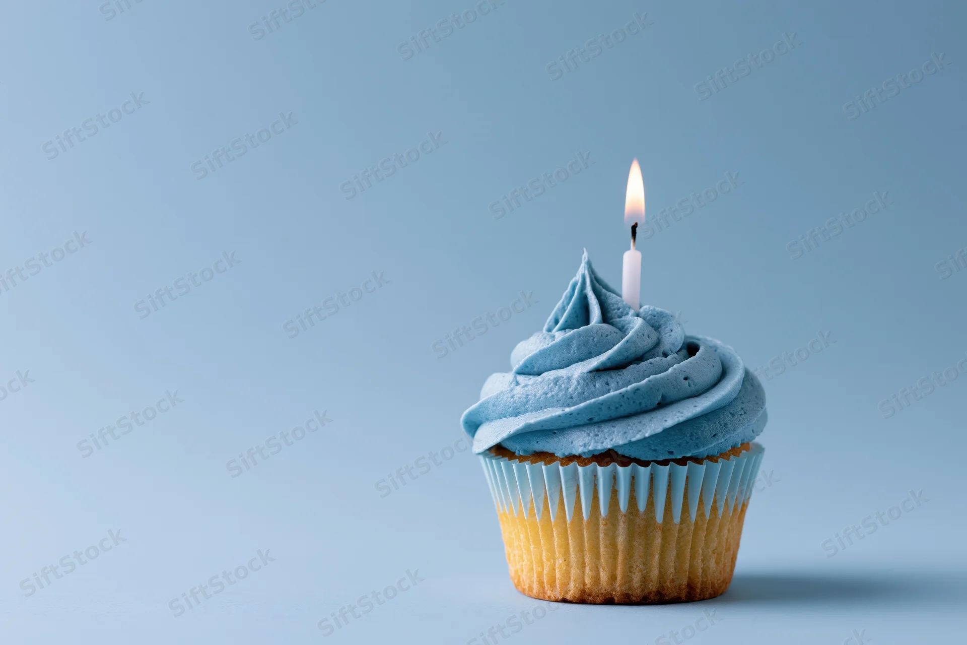 Single cupcake with blue swirled frosting and lit candle on plain blue background