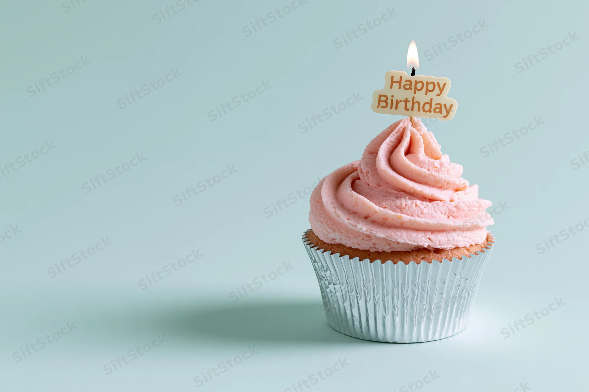 Single cupcake with pink frosting and lit birthday candle on a light blue surface