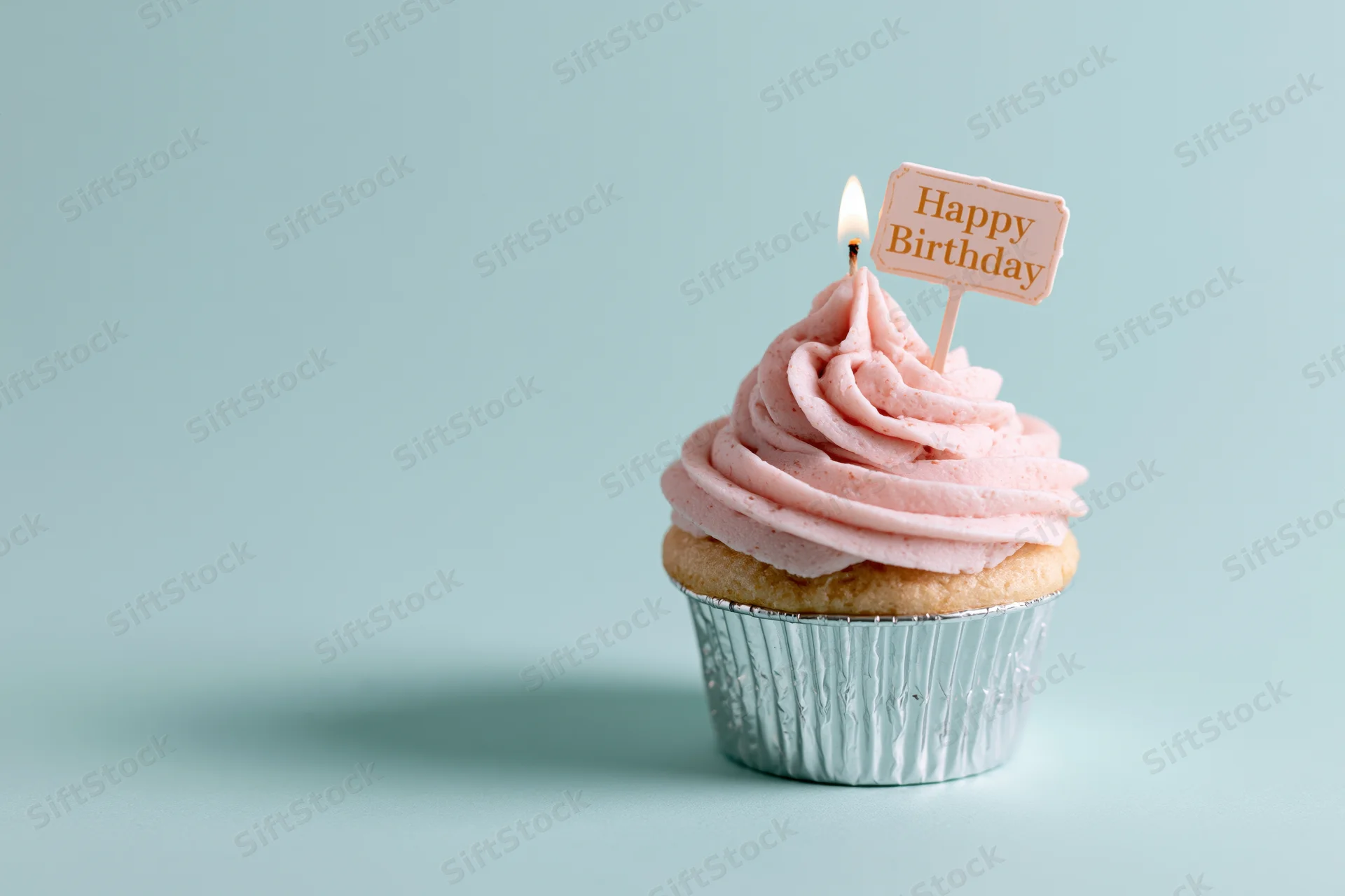 Single cupcake with pink frosting and lit candle on mint background