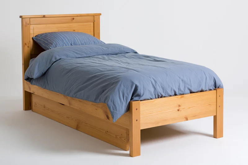 Wooden bed with headboard and under-bed drawer neatly arranged in a studio setting