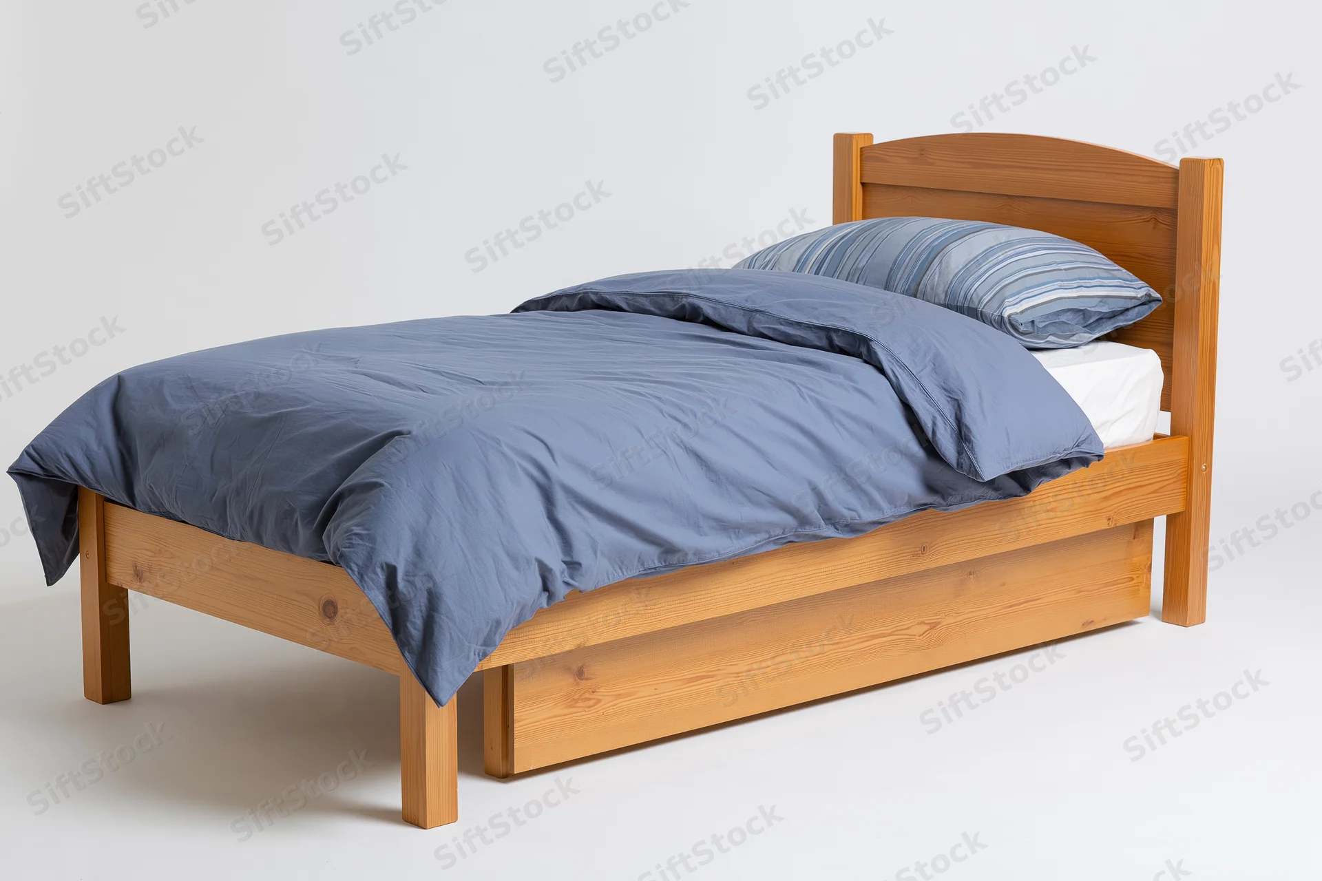 Wooden bed with headboard and under-bed drawer neatly arranged with blue bedding on white background