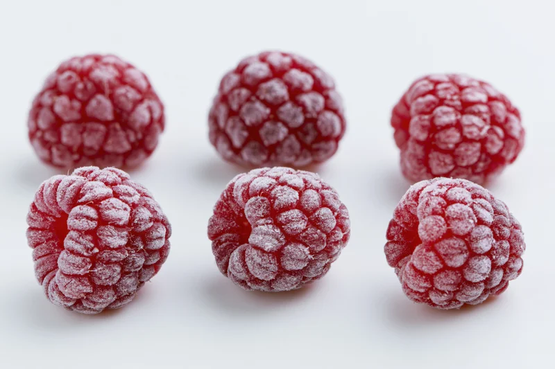 Six frozen raspberries arranged in two rows on a white surface