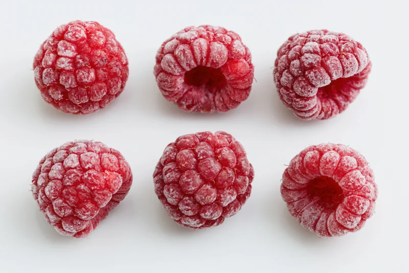 Six frozen raspberries arranged in two rows on a white background