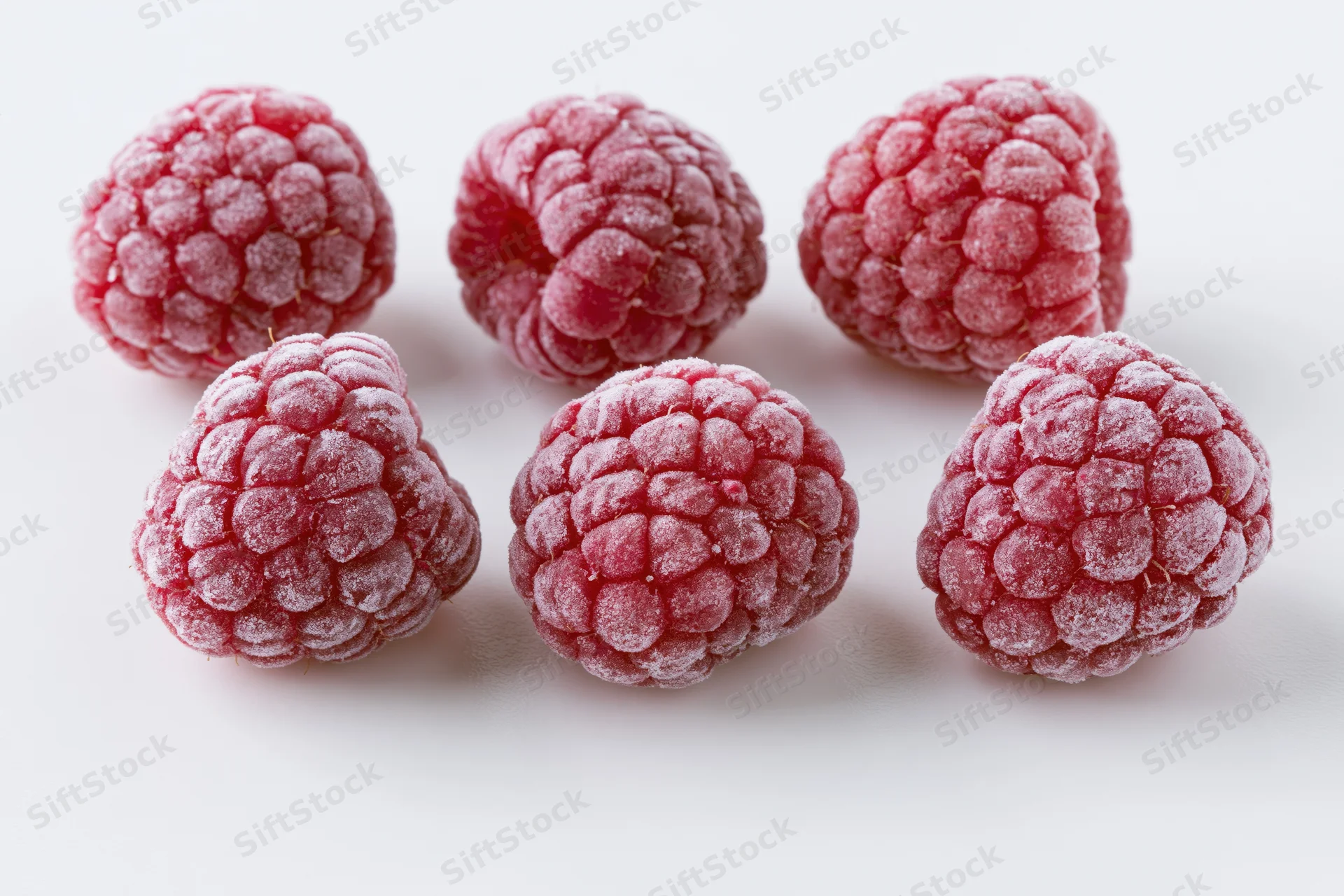 Six frozen raspberries arranged in two rows on a white surface