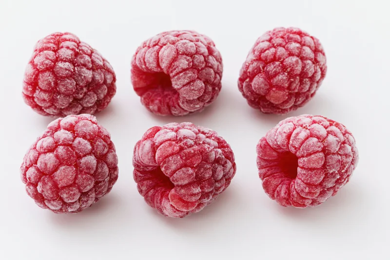 Six frozen raspberries arranged in two rows on a white surface