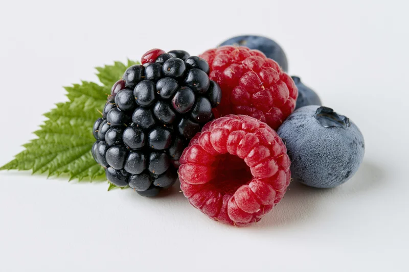 Cluster of fresh blackberries, raspberries and blueberries with a green leaf on white background