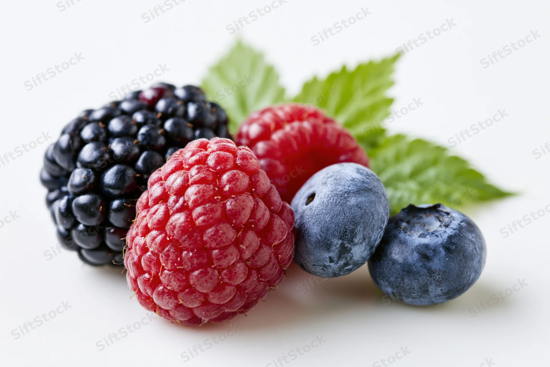 Cluster of fresh blackberries, raspberries and blueberries with green leaves on white background