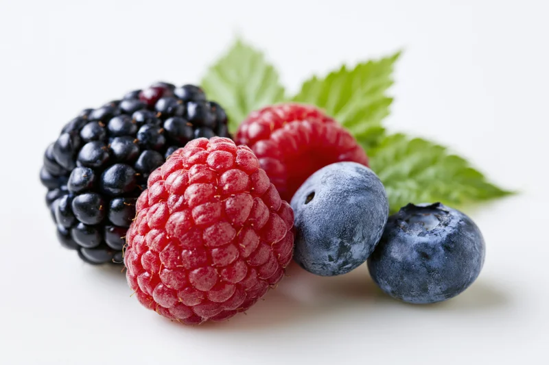 Cluster of fresh blackberries, raspberries and blueberries with green leaves on white background