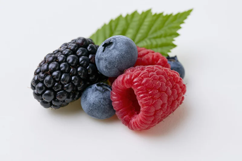 Small cluster of fresh blackberry raspberry and blueberries with a green leaf on white background