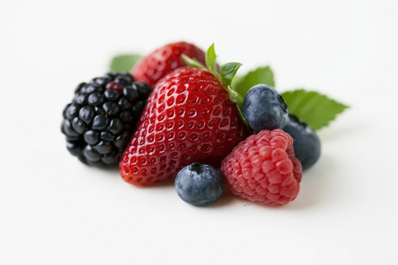 Small cluster of fresh mixed berries including strawberry, blackberry, raspberry and blueberry with green leaves on white background