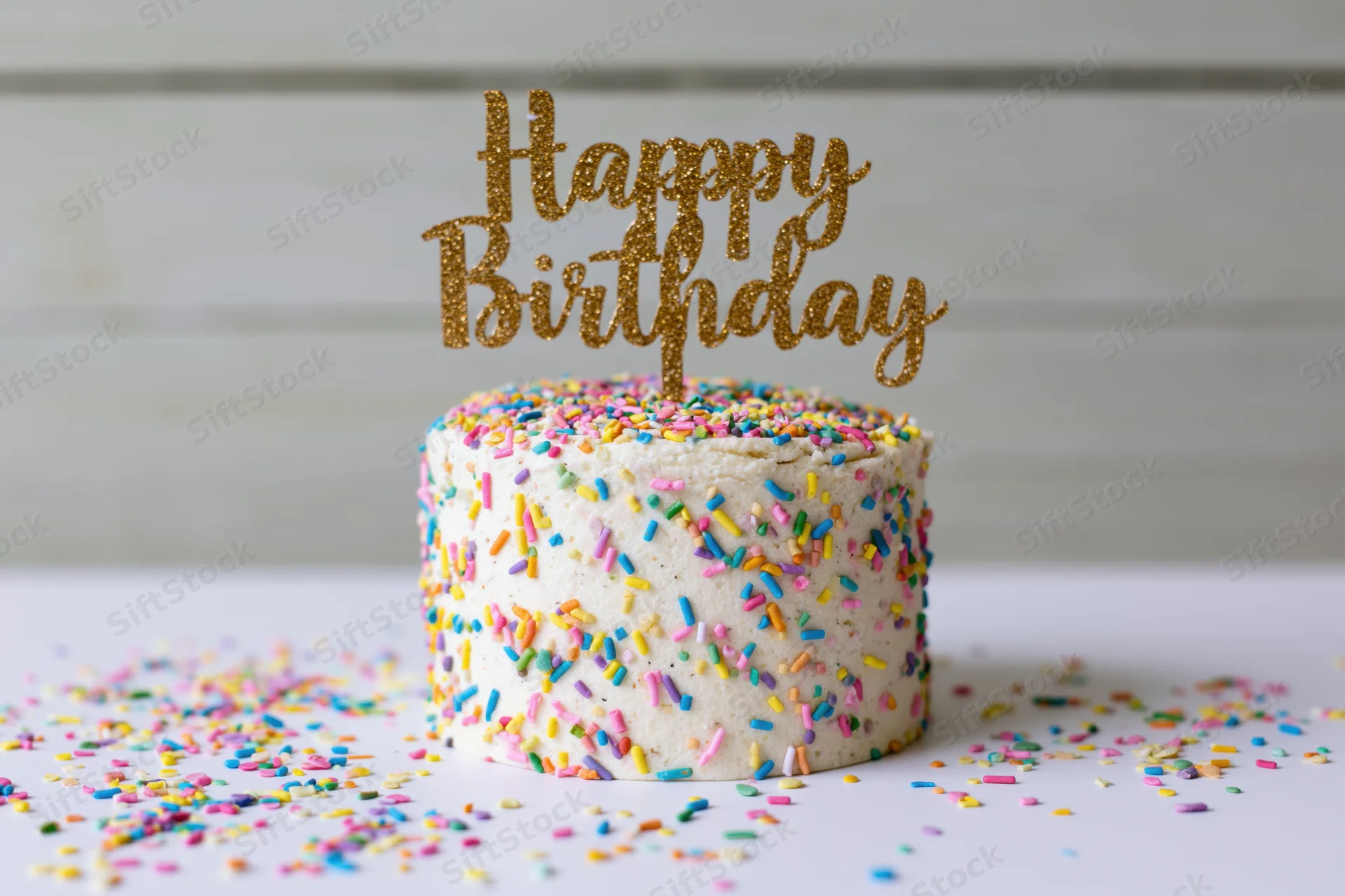 Small white frosted birthday cake with gold glitter topper and colorful sprinkles on white surface