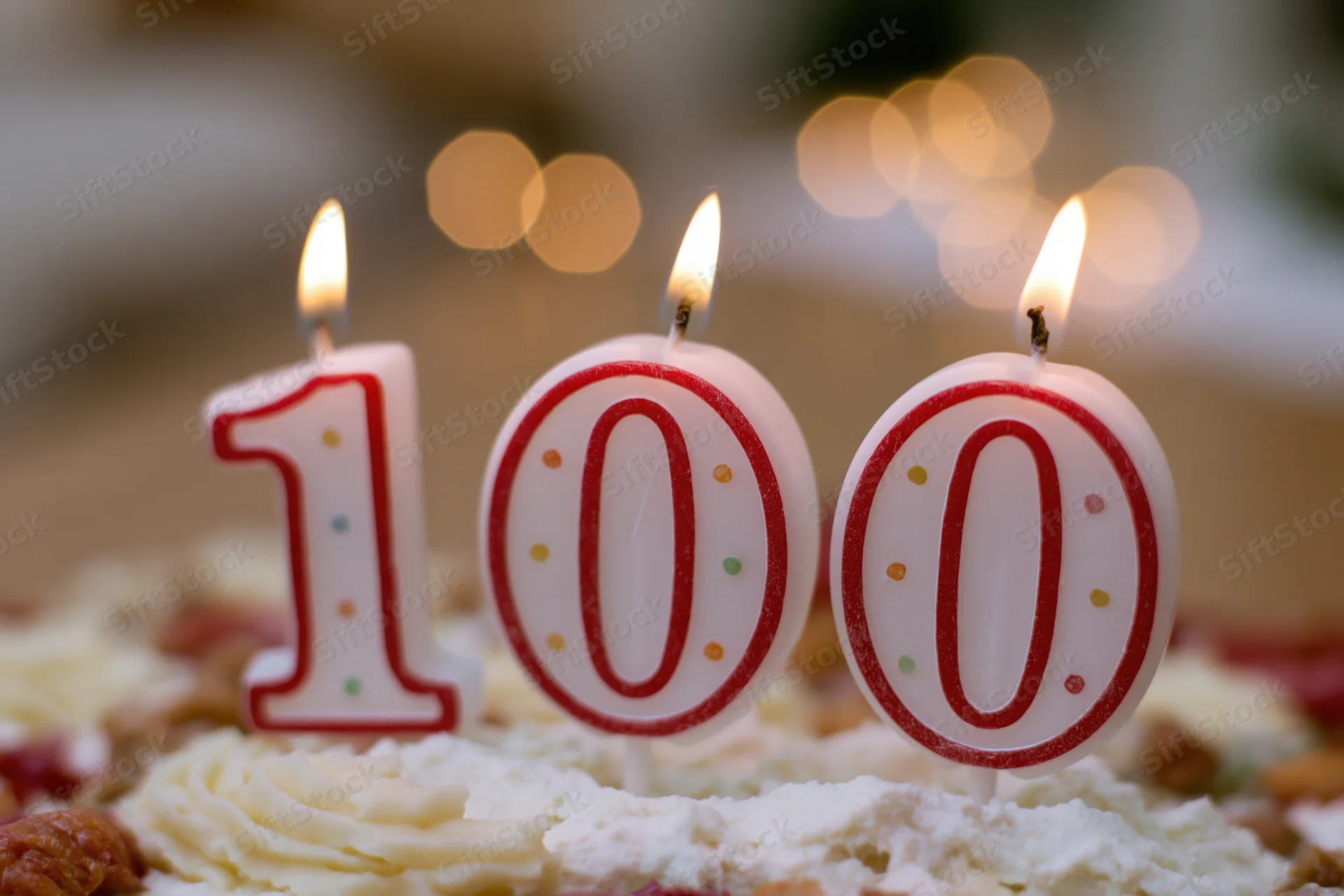 Three lit number candles spelling 100 on a frosted birthday cake