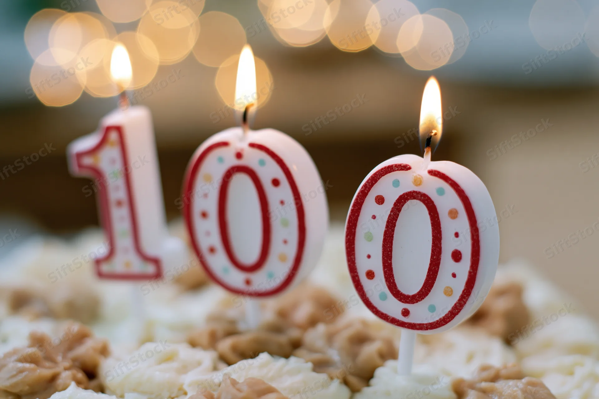 Three lit number candles spelling 100 on a frosted birthday cake