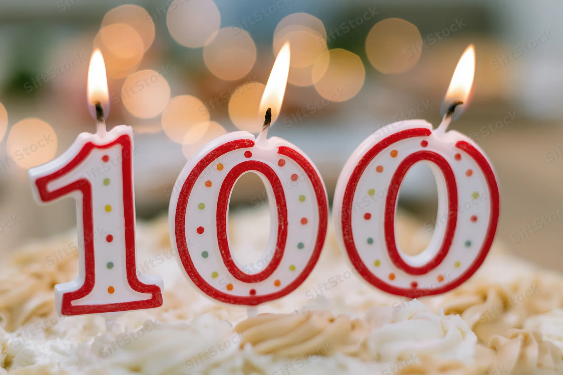 Three lit number candles spelling 100 on a frosted birthday cake