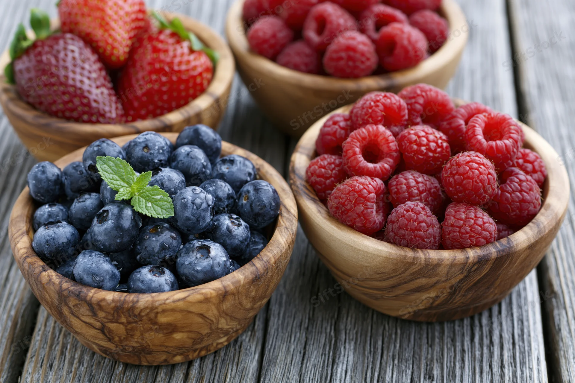 Blueberries, raspberries and strawberries in rustic olive wood bowls on a weathered wooden table
