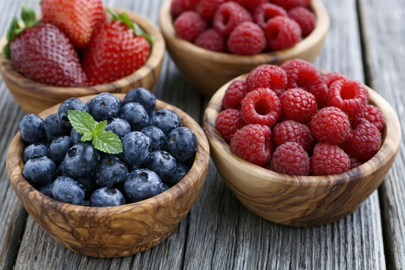 Blueberries, raspberries and strawberries in rustic olive wood bowls on a weathered wooden table