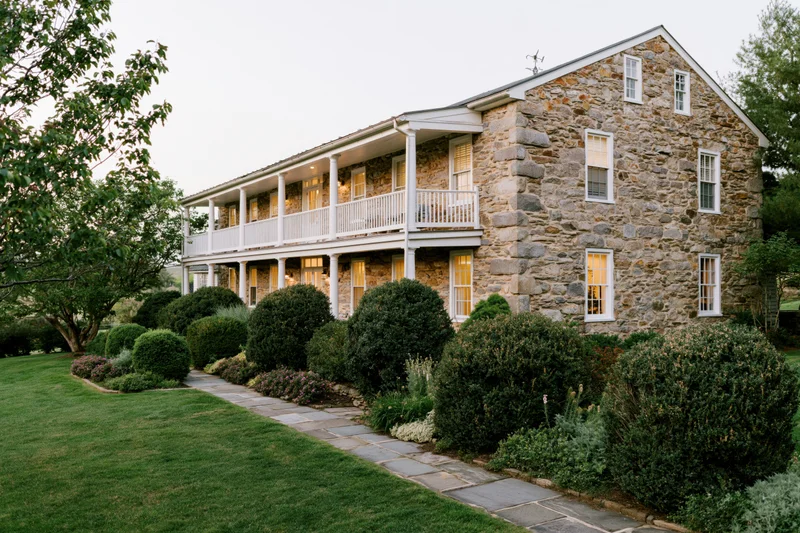 Two-story historic stone farmhouse with white balconies and garden pathway at dusk