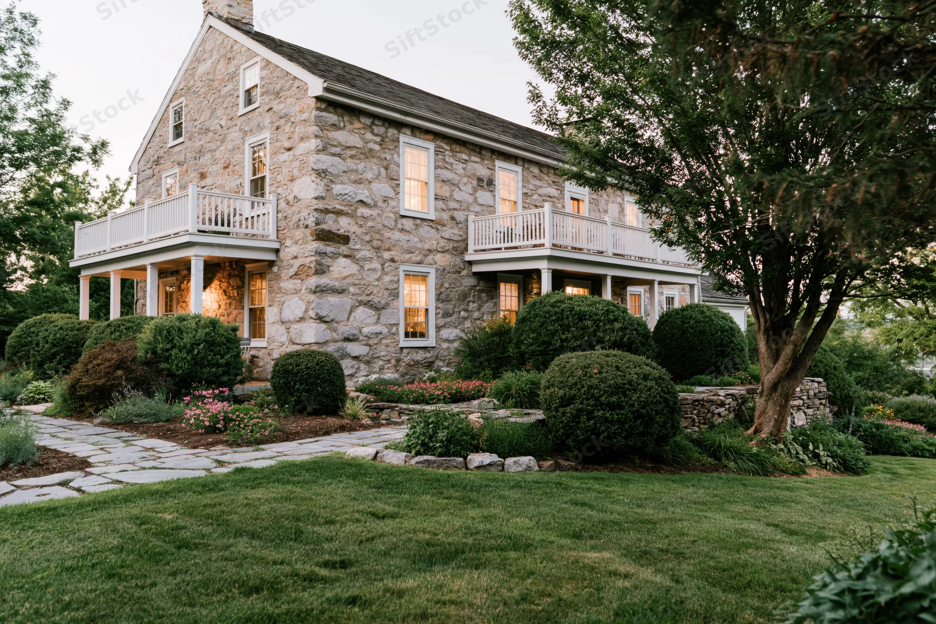 Two-story historic stone farmhouse with white balconies and garden at dusk