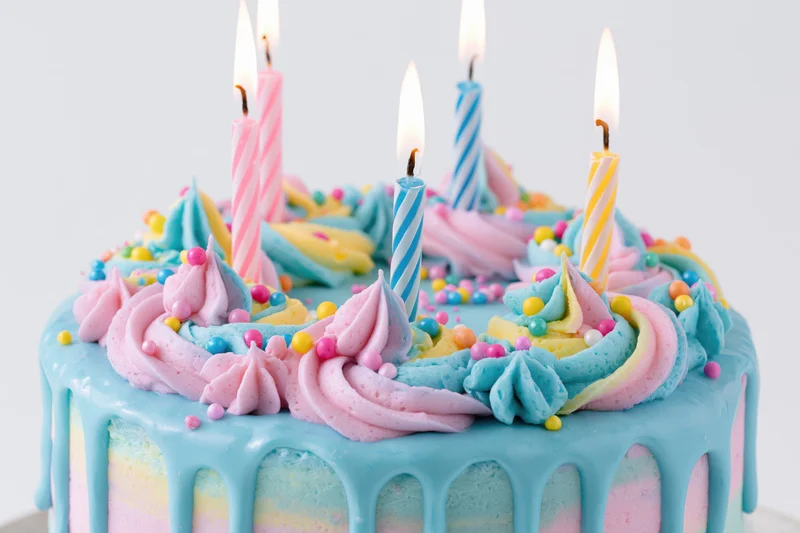 Colorful birthday cake with lit striped candles and pastel frosting drip