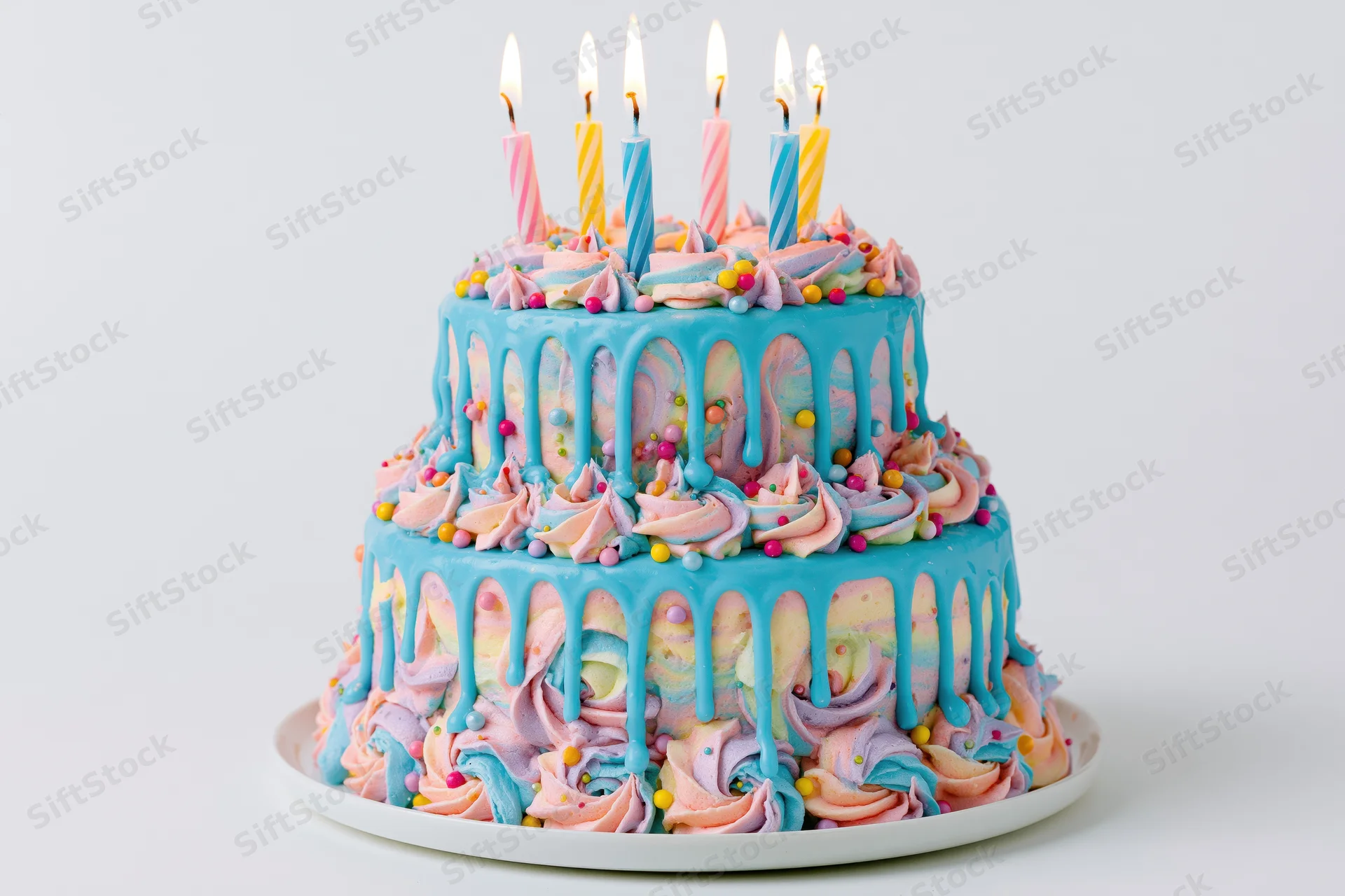 Two-tier birthday cake with lit striped candles and pastel frosting on a white plate