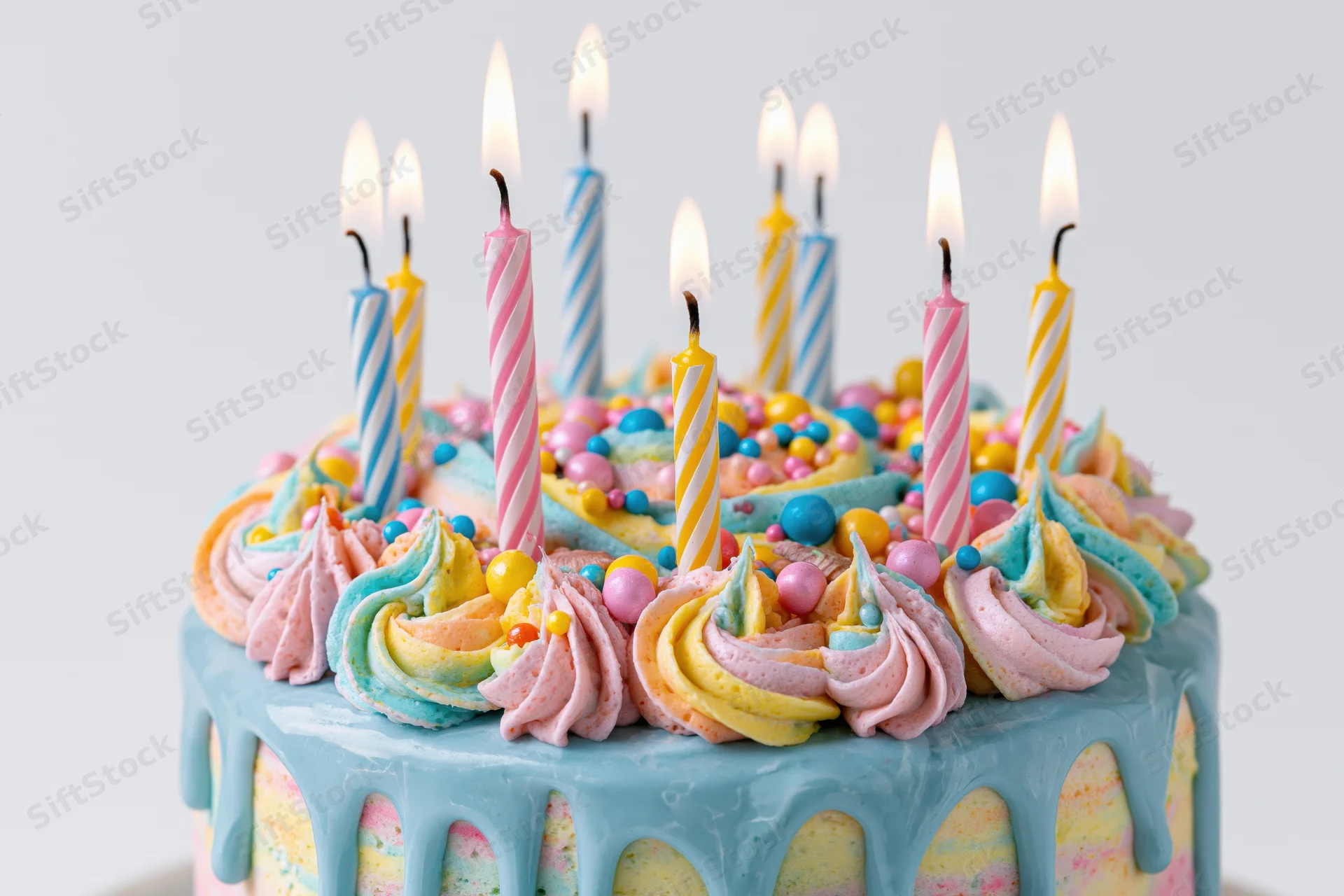 Colorful two-tier birthday cake with lit striped candles and pastel frosting swirls