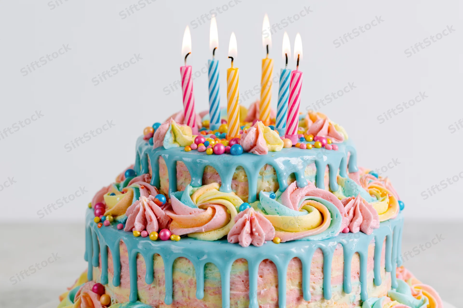 Two-tier birthday cake with lit striped candles and colorful frosting drips