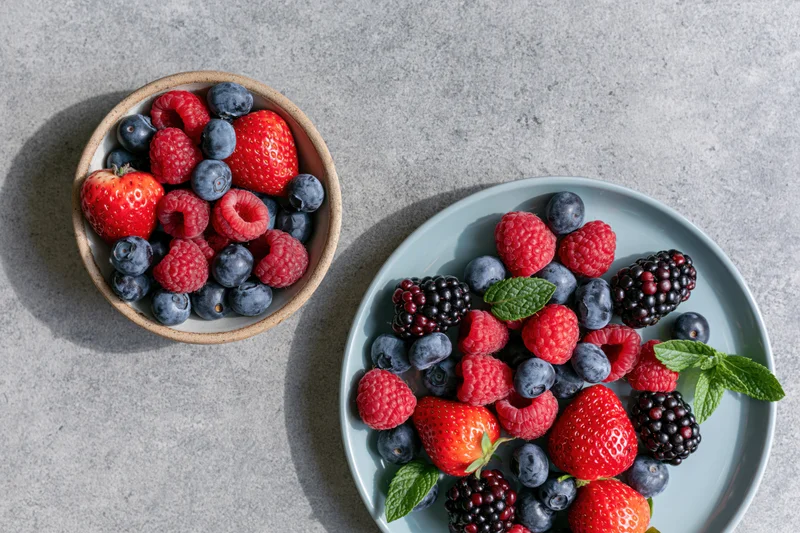 Mixed berries in ceramic dishes on gray surface, overhead view