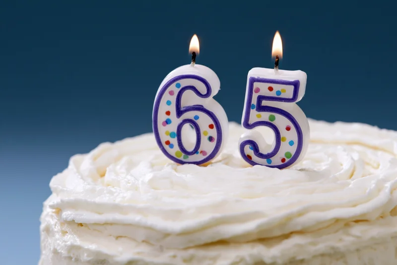 Birthday cake with lit number candles reading sixtyfive on white frosting