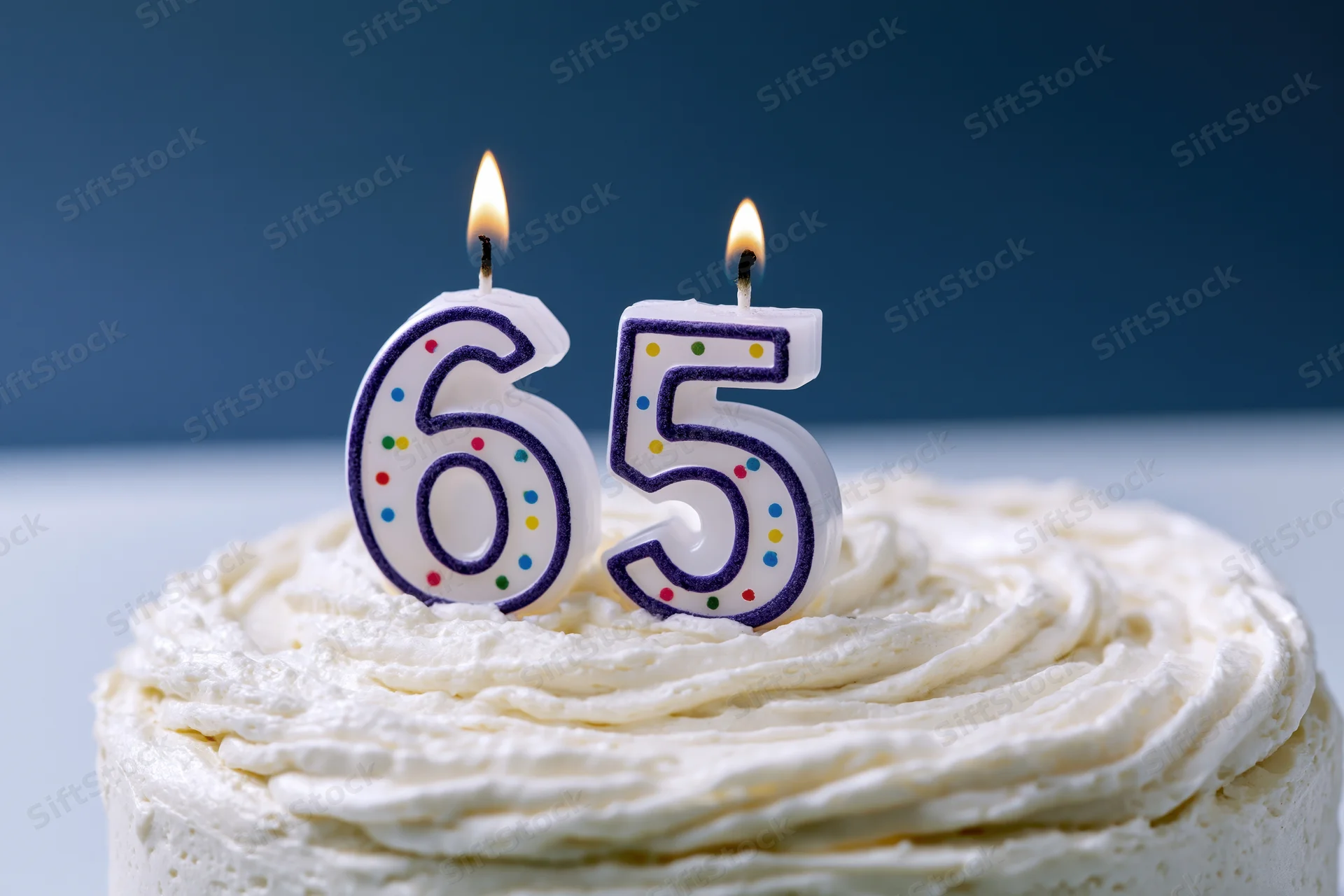 White frosted birthday cake with lit number 65 candles on top