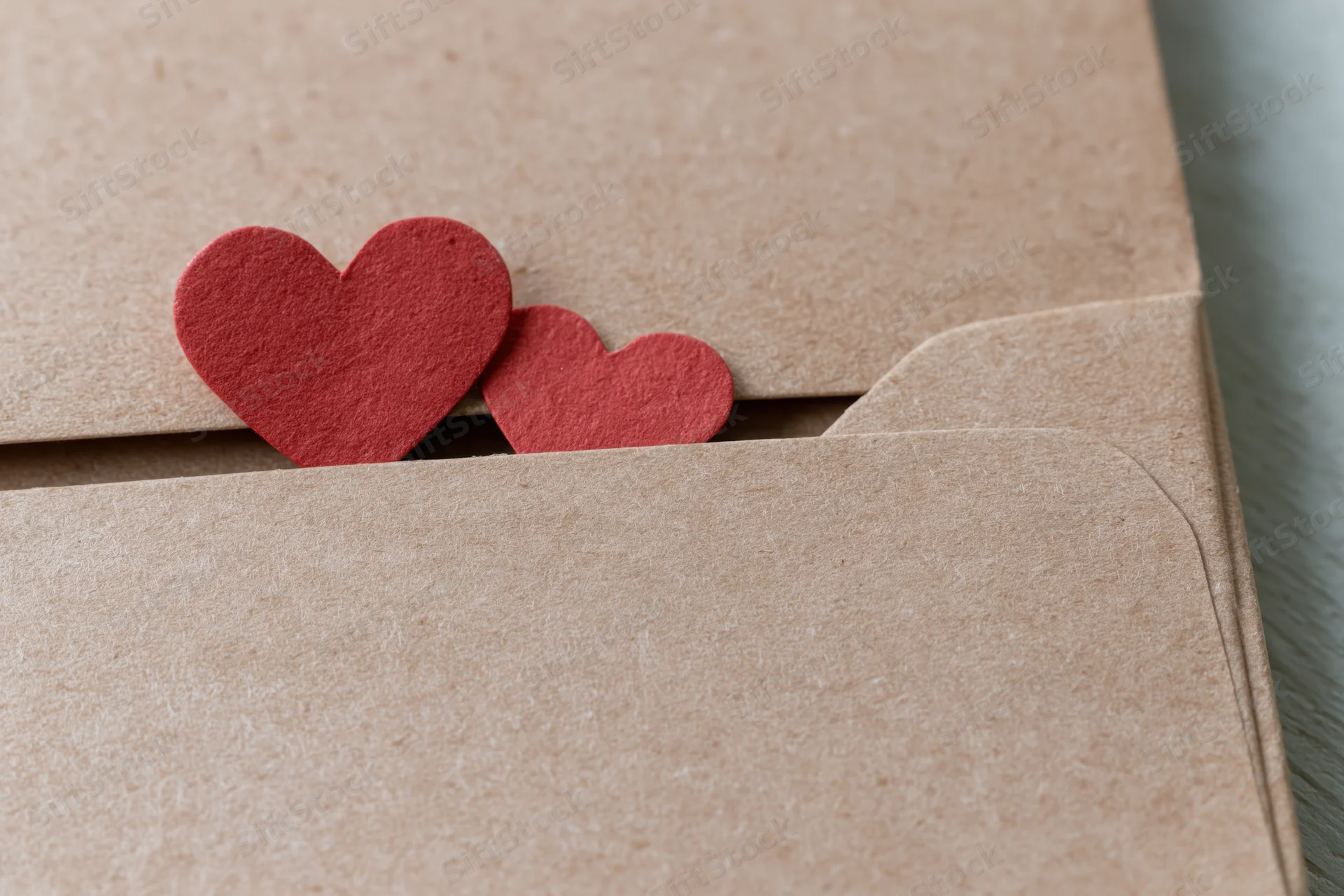 Two red paper hearts peeking from a kraft envelope flap