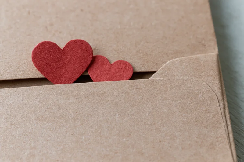 Two red paper hearts peeking from a kraft envelope flap