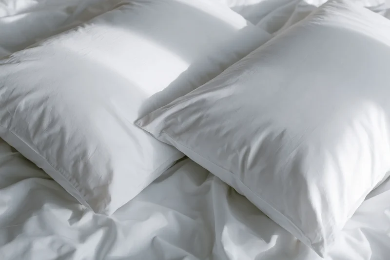 Two white pillows resting on a rumpled white bedsheet in a bedroom