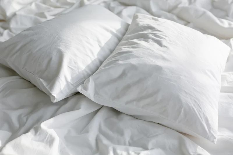 Two white pillows resting on an unmade bed with wrinkled white sheets