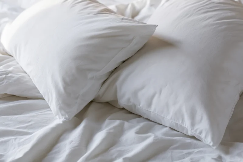 Two white pillows resting on an unmade bed with wrinkled white sheets