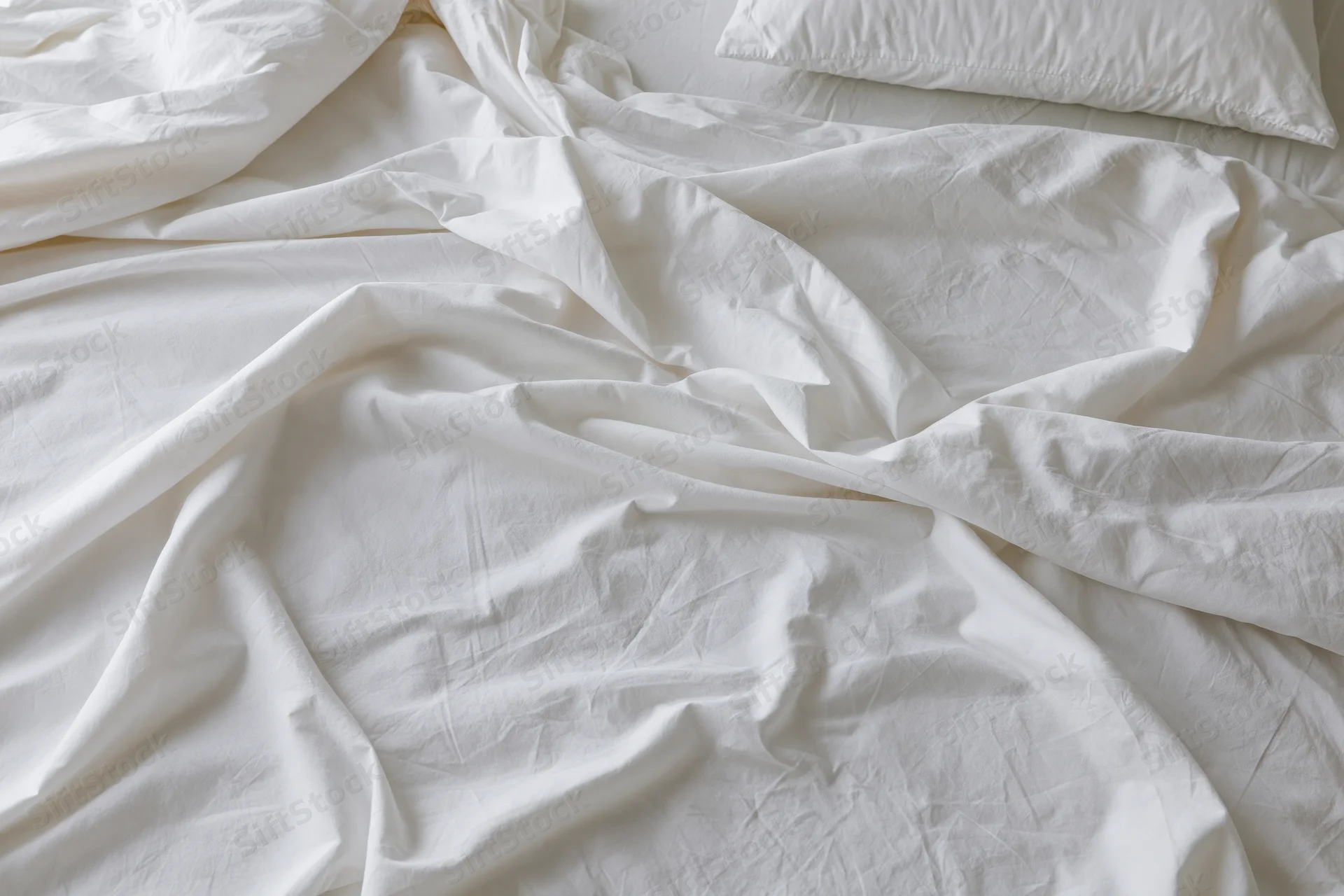 Unmade bed with crumpled white cotton sheets and a single pillow in a bedroom