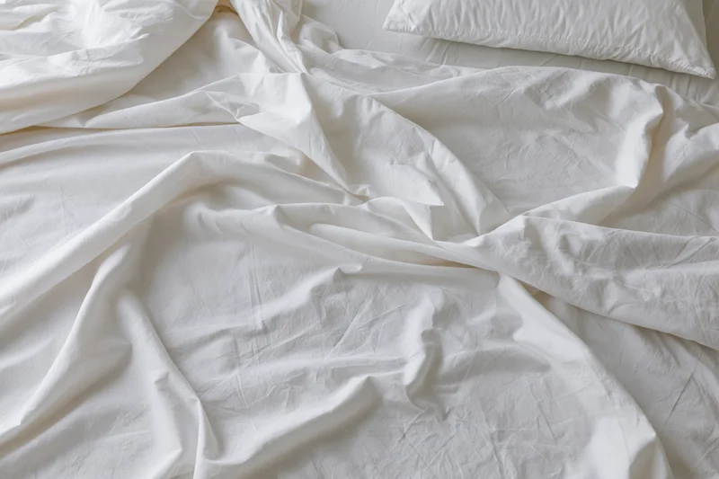 Unmade bed with crumpled white cotton sheets and a single pillow in a bedroom