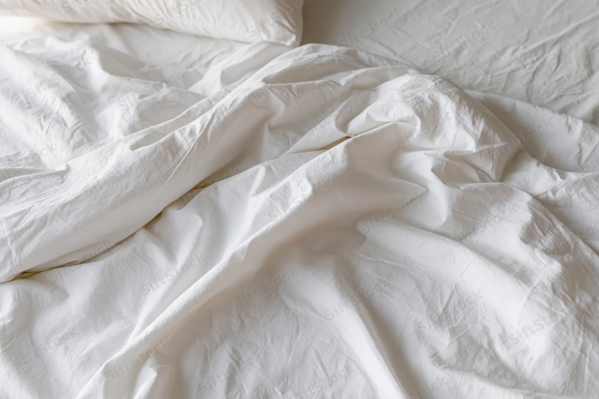 Unmade bed with crumpled white cotton sheets and a pillow in a bedroom