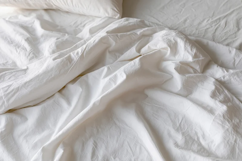 Unmade bed with crumpled white cotton sheets and a pillow in a bedroom