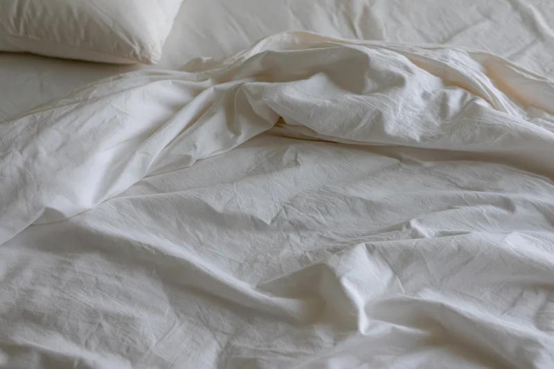 Unmade bed with crumpled white cotton sheets and a single pillow in a bedroom