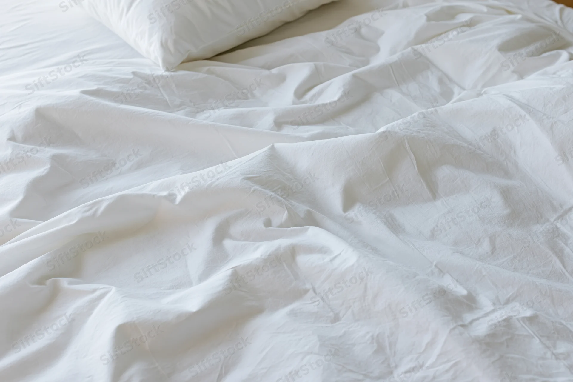 Unmade bed with crumpled white cotton sheets and a single pillow in a bedroom