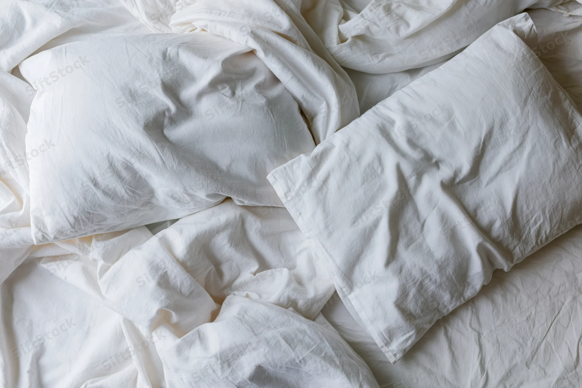 Unmade bed with crumpled white cotton sheets and two rumpled pillows in a bedroom