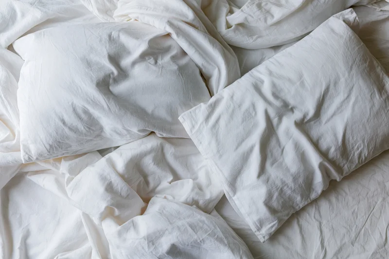 Unmade bed with crumpled white cotton sheets and two rumpled pillows in a bedroom