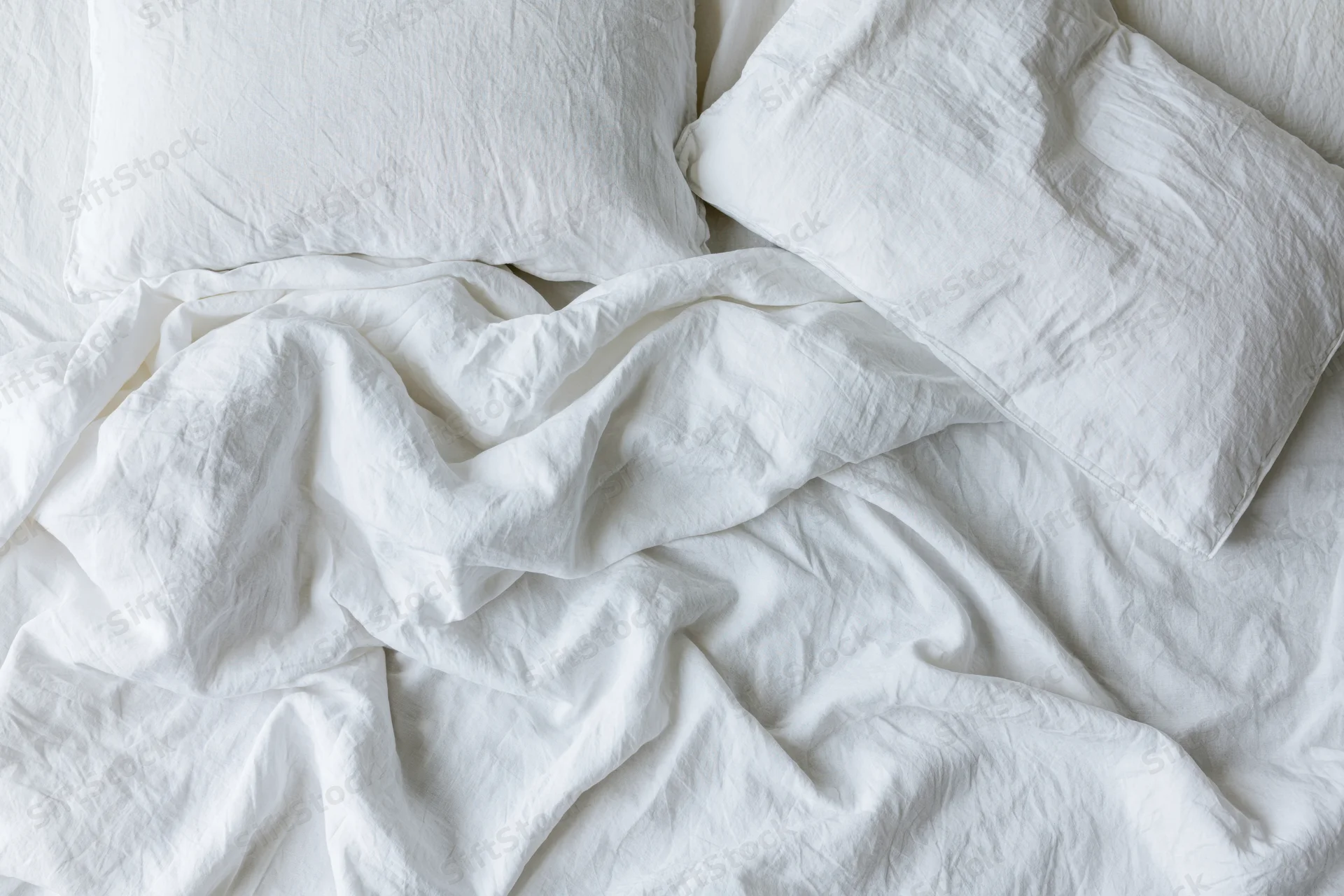 Unmade bed with crumpled white cotton sheets and two rumpled pillows