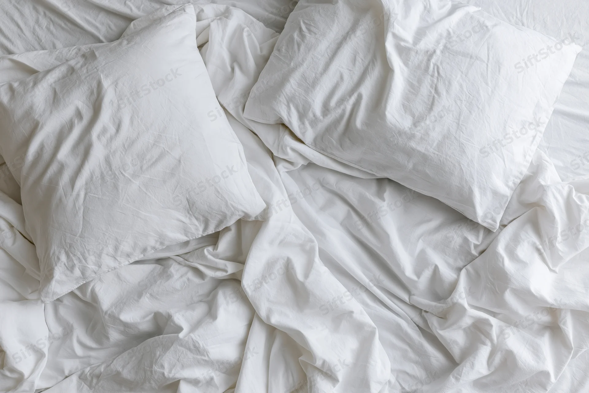 Unmade bed with crumpled white cotton sheets and two rumpled pillows in a bedroom